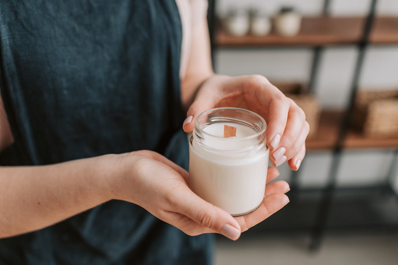 about-us-02 Close-up of hands holding a jar candle indoors on a softly focused background.