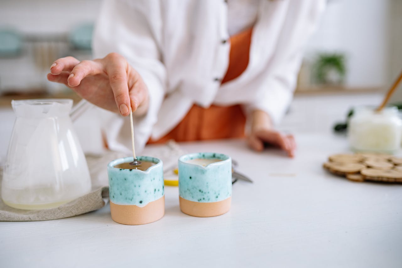 services-02 Close-up of hands making handmade candles using soy wax in decorative containers.
